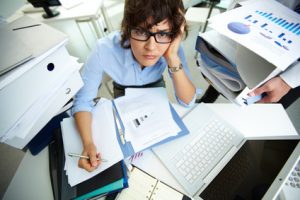 Perplexed accountant doing financial reports being surrounded by huge piles of documents